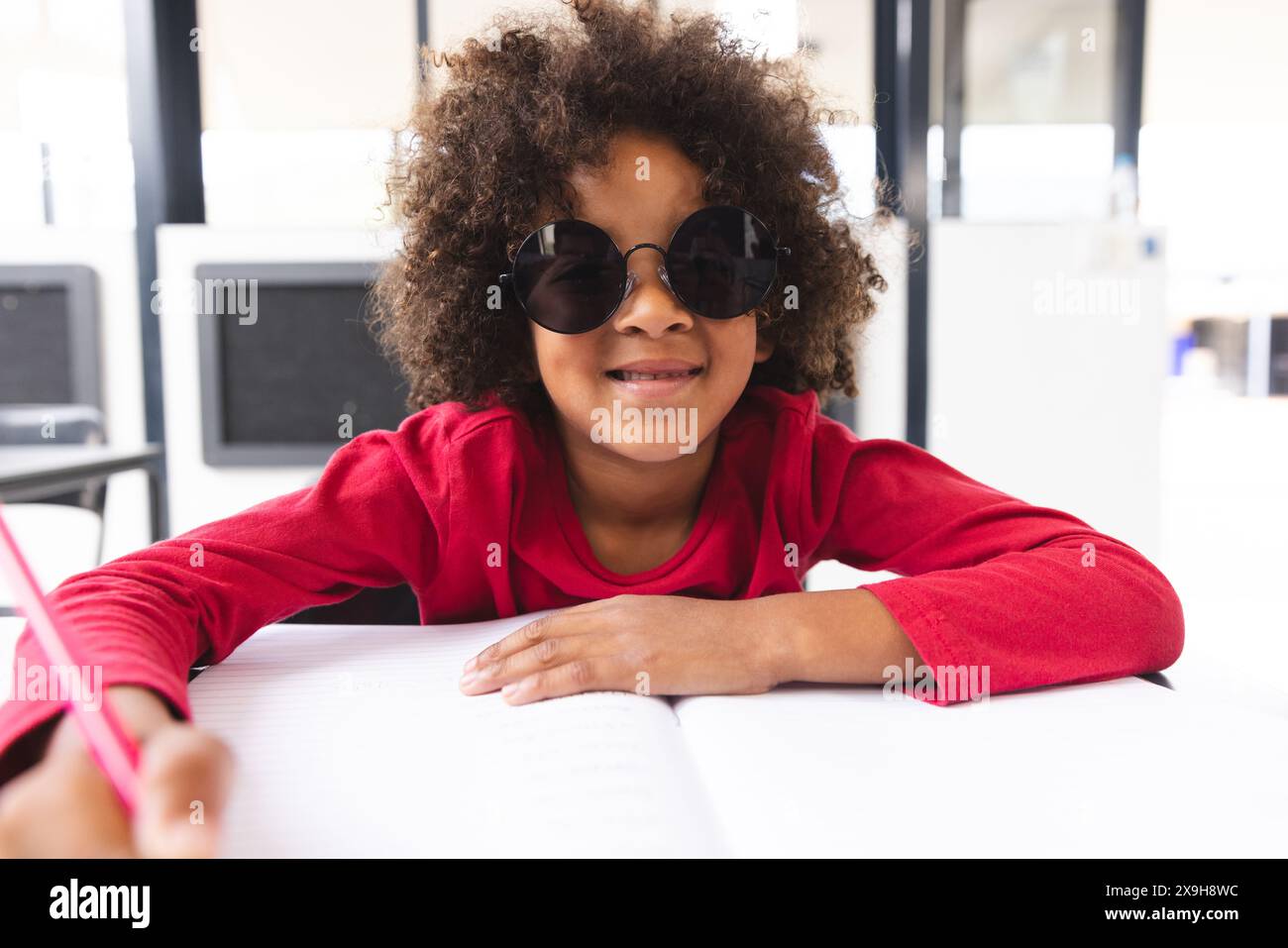 In der Schule saß ein junger männlicher Schüler mit Sonnenbrille an einem Schreibtisch im Klassenzimmer Stockfoto