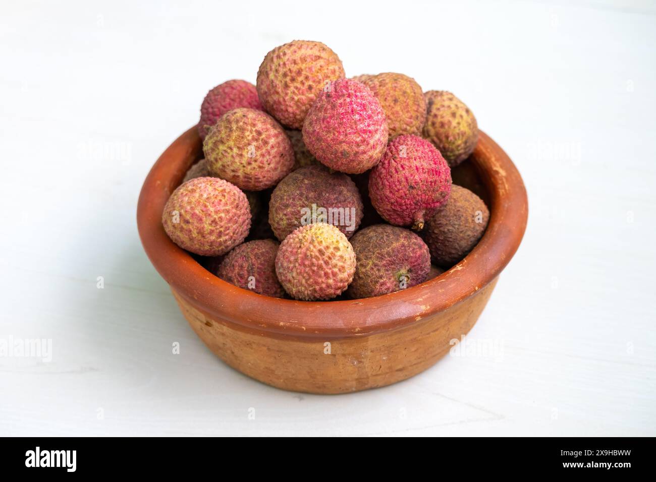 Ein Tontopf gefüllt mit köstlichen Reifen Litschis. Die Litschis haben eine rötlich-braune, strukturierte Haut. Litschis sind eine gesunde tropische Frucht. Stockfoto