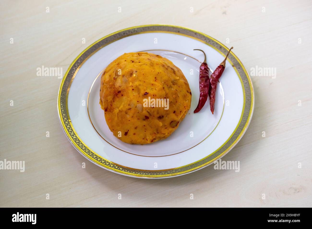 Köstliches Aloo Bhorta auf einem weißen Teller auf hölzernem Hintergrund. Alu Vorta ist ein traditionelles Essen aus Bangladesch und der Region Bengalen in Indien. Stockfoto