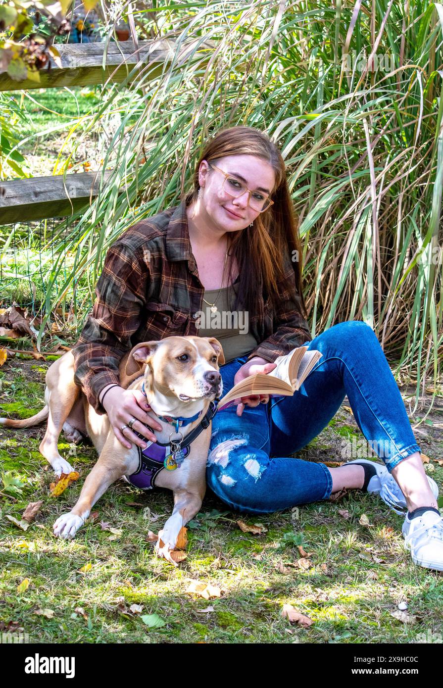 Eine hübsche junge Frau sitzt mit ihrem Anfallswarnhund und liest ein gutes Buch Stockfoto