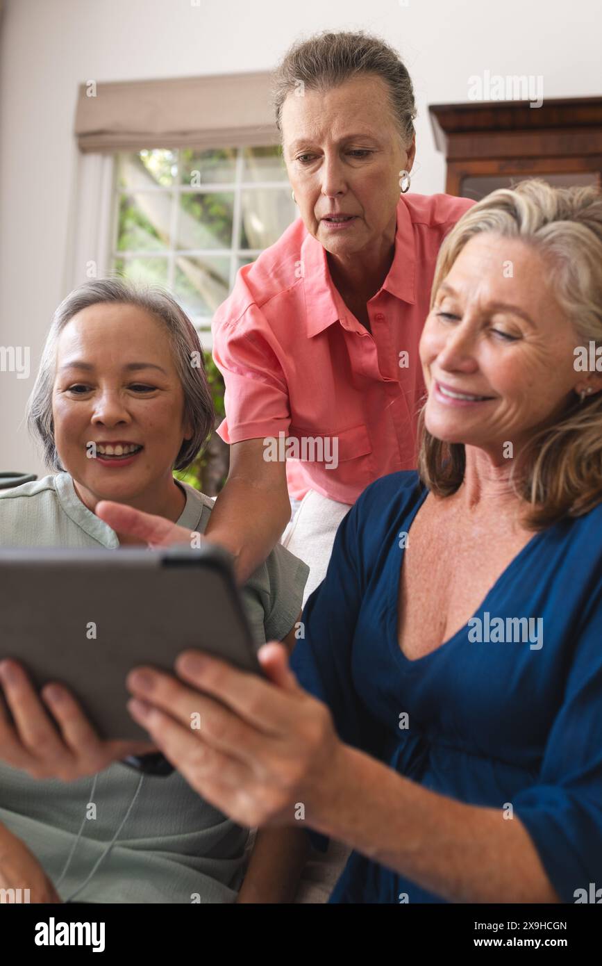 Verschiedene ältere Freundinnen teilen sich zu Hause ein Tablet, alle lächeln zusammen Stockfoto