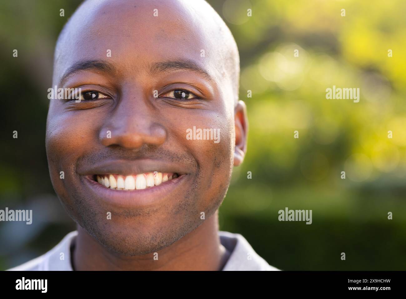 Draußen lächelt ein junger Afroamerikaner mit üppigem Grün Stockfoto