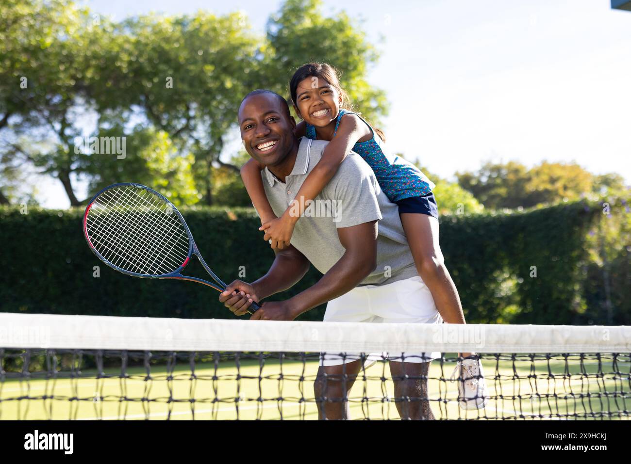 Im Freien gibt es vielfältige Vater und Tochter auf dem Tennisplatz mit üppig grünen Bäumen Stockfoto
