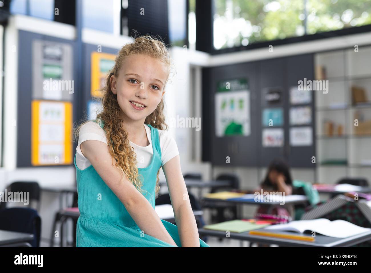 Ein weißes Mädchen mit lockigen blonden Haaren lächelt in einem Klassenzimmer mit Kopierraum Stockfoto