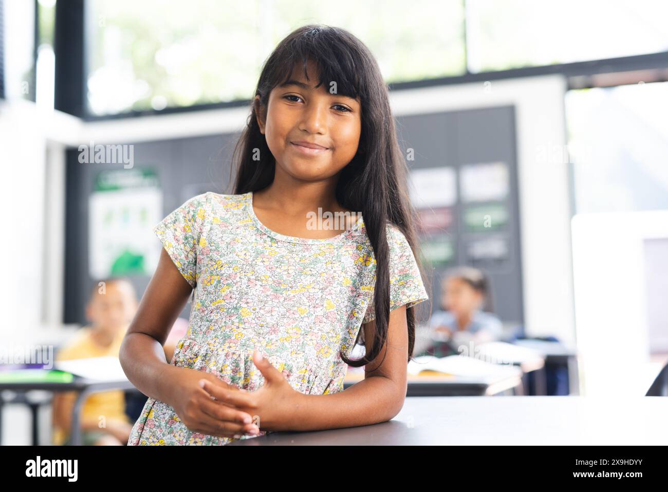 Ein birassisches Mädchen mit langen braunen Haaren steht lächelnd in einem Klassenzimmer Stockfoto