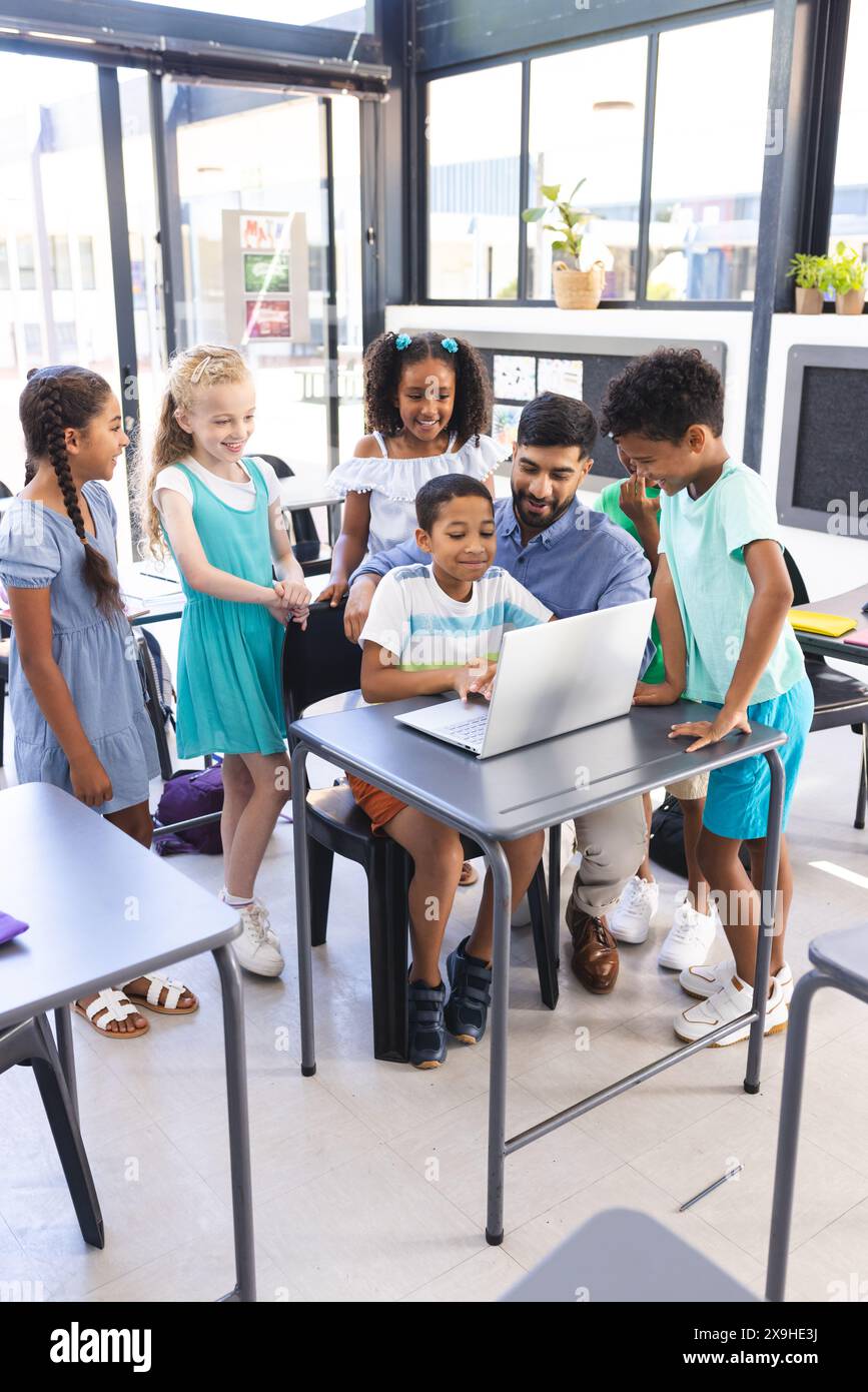 Ein junger asiatischer Lehrer führt die Kinder durch den Laptop Stockfoto