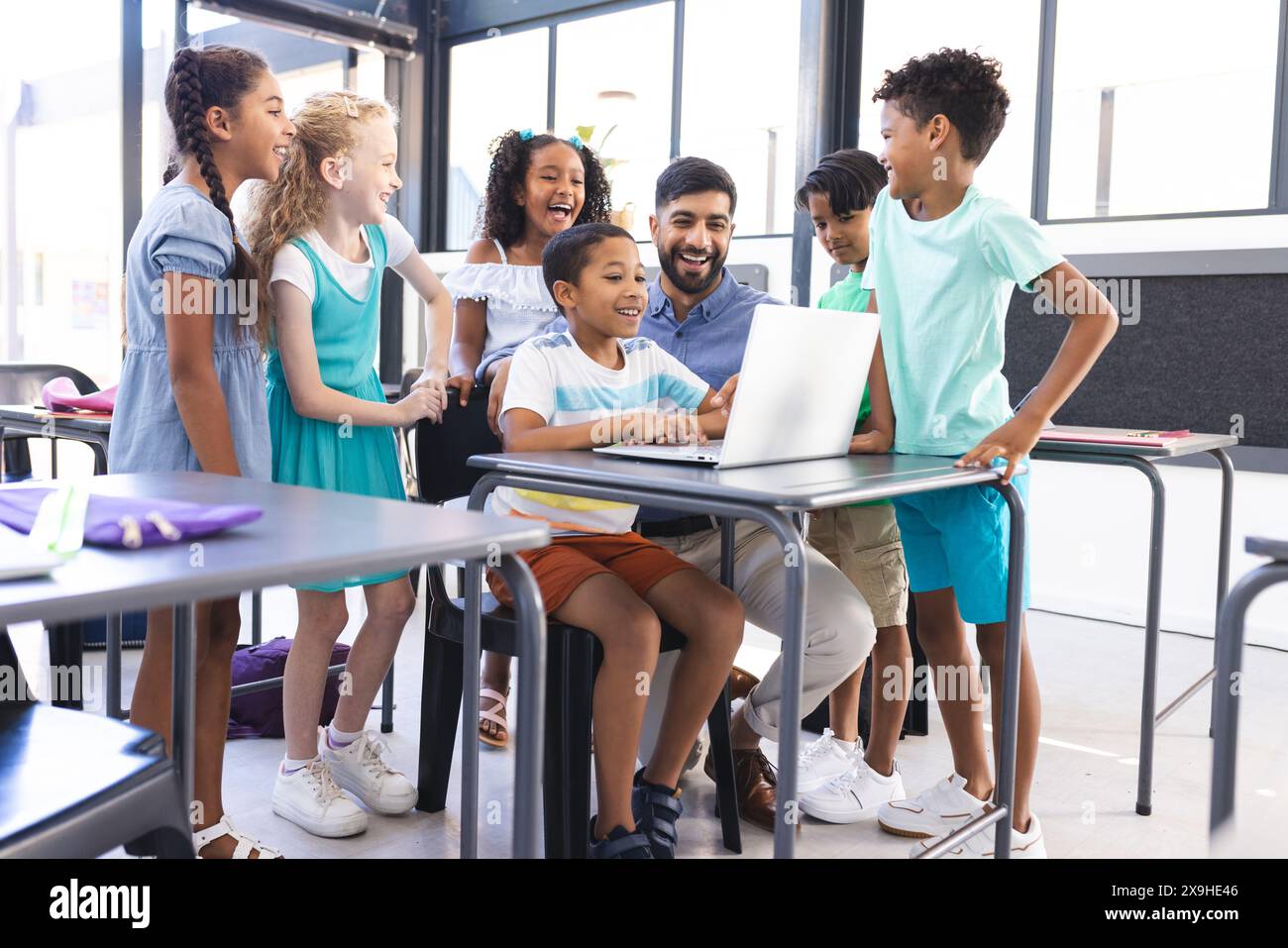 Ein junger asiatischer Lehrer und Kinder drängen sich am Laptop Stockfoto