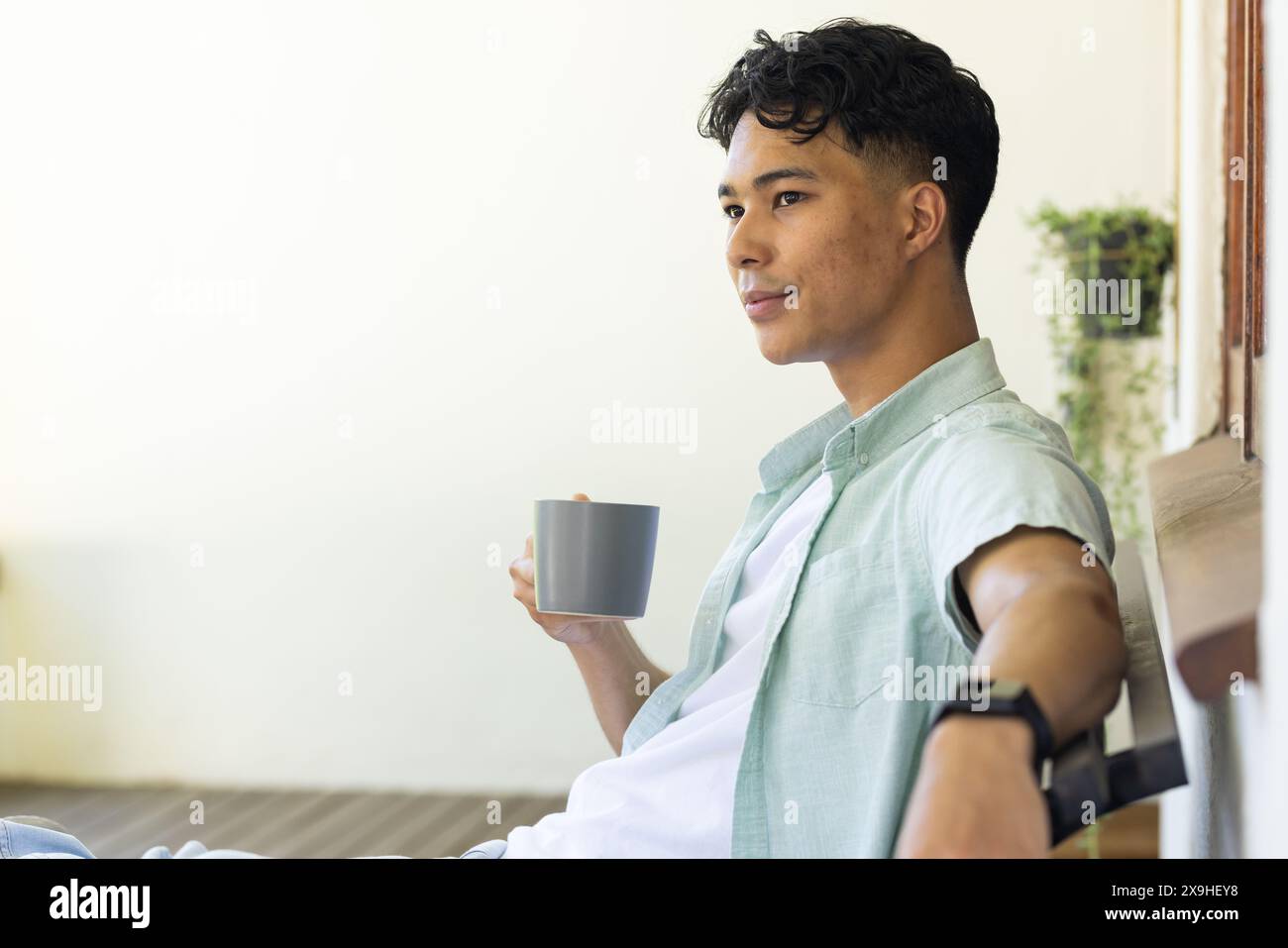 Draußen, birassischer junger Mann mit Tasse, entspannend auf einer Bank, Kopierraum Stockfoto