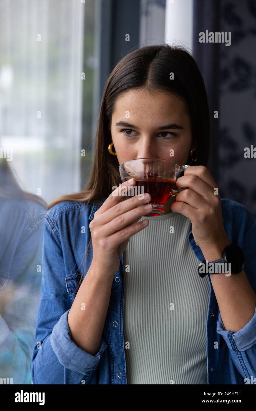 Zu Hause genießt die junge kaukasische Frau eine Tasse Tee, sieht entspannt und zufrieden aus. Sie befindet sich in gemütlicher Spa-Umgebung mit sanfter Beleuchtung und einer ruhigen A Stockfoto