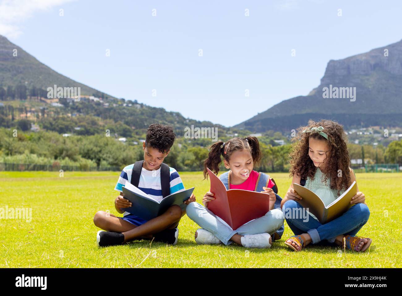 Birassische Kinder lesen Bücher im sonnigen Feld, Kopierraum Stockfoto