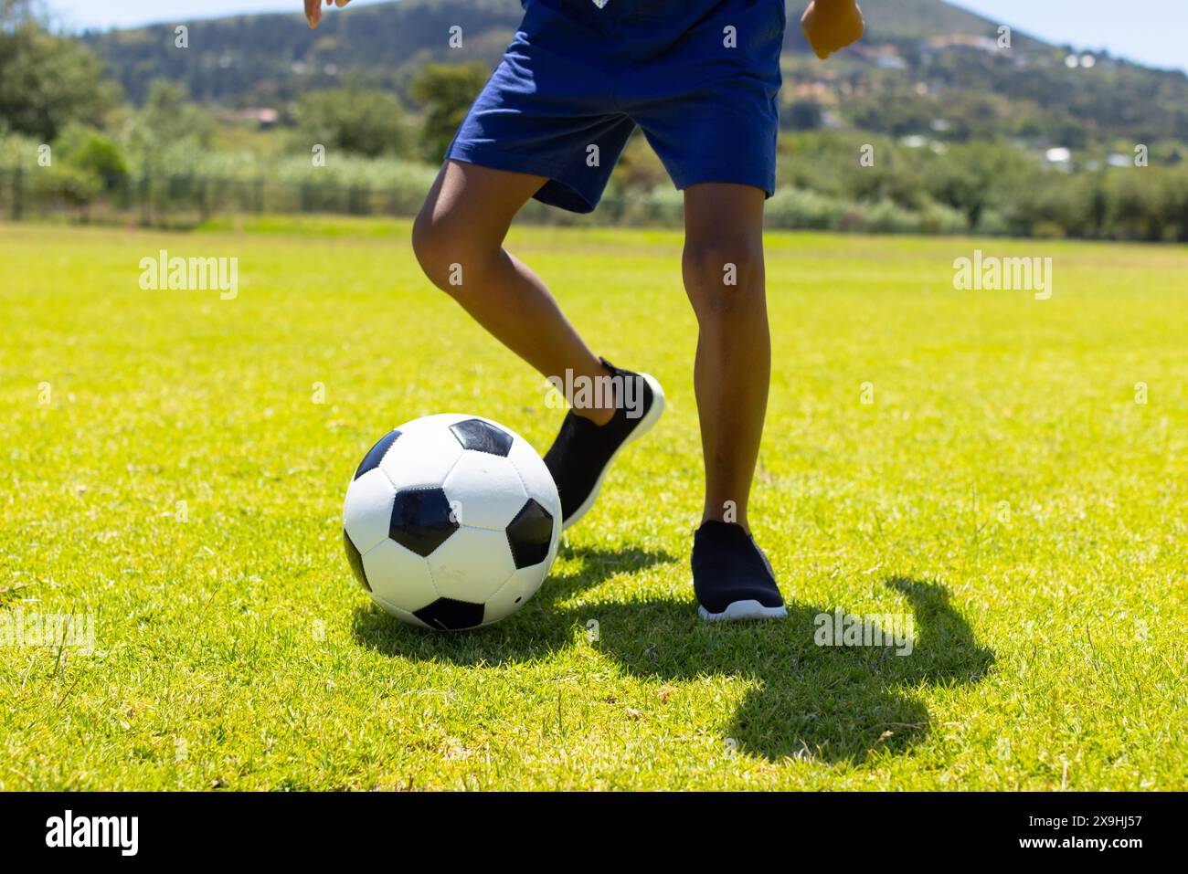 Birassischer Junge spielt Fußball auf einem sonnigen Feld und zeigt seine Fähigkeiten mit einem schwarz-weißen Ball Stockfoto