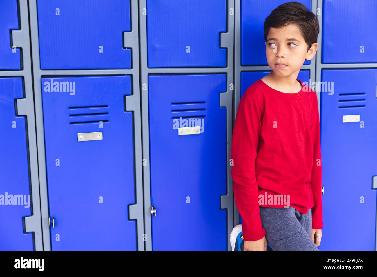 In der Schule stand ein junger, birassischer Junge draußen an blauen Schließfächern, blickte weg, mit Kopierraum Stockfoto
