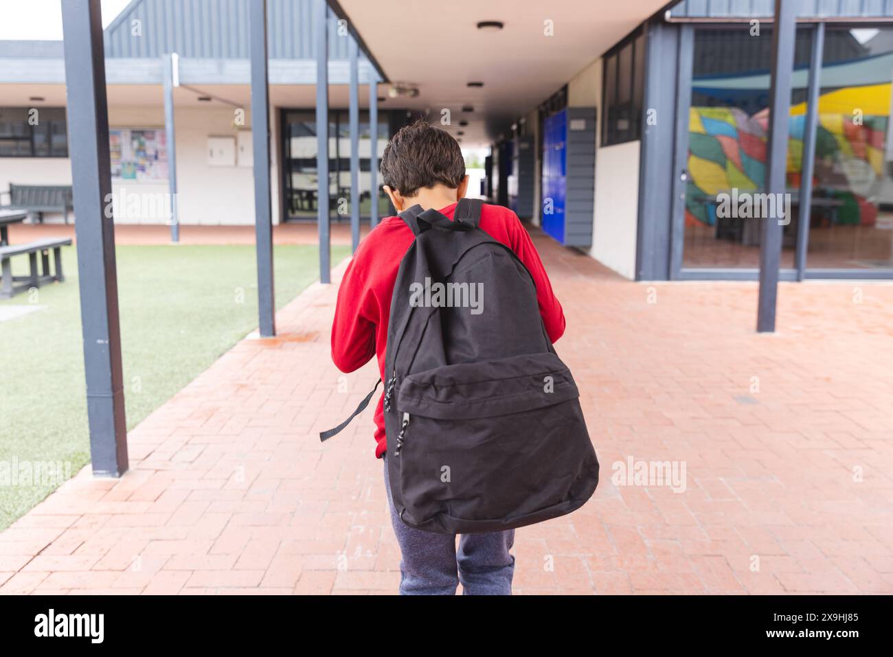 In der Schule ging ein junger männlicher Student mit rotem Hoodie und Jeans draußen Stockfoto