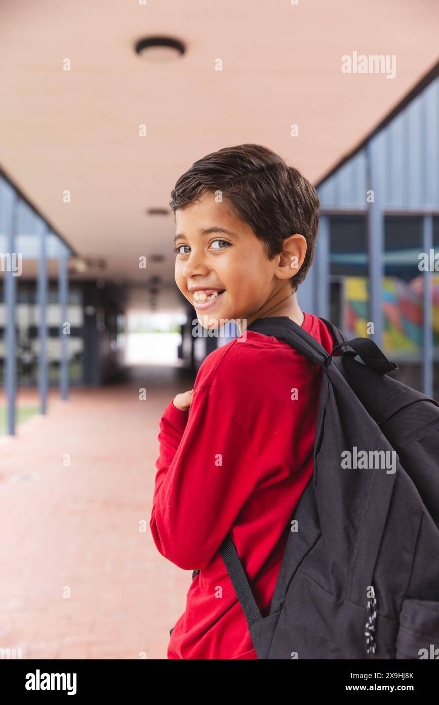 In der Schule lächelt ein junger männlicher Student mit rotem Hemd draußen Stockfoto