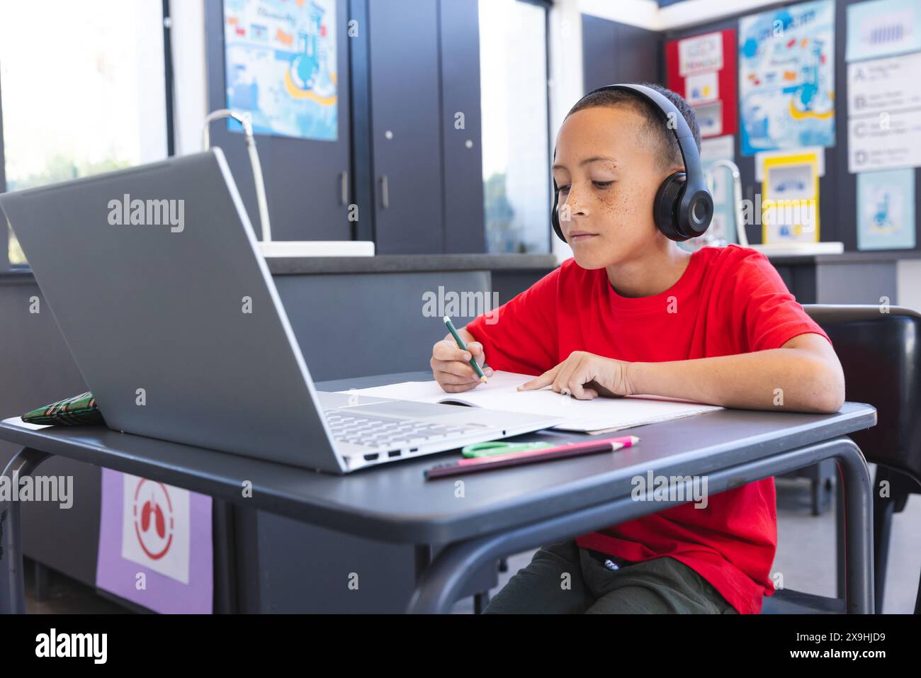 Biracial Boy studiert intensiv in einer Schulklasse mit einem Laptop, mit Kopierraum Stockfoto