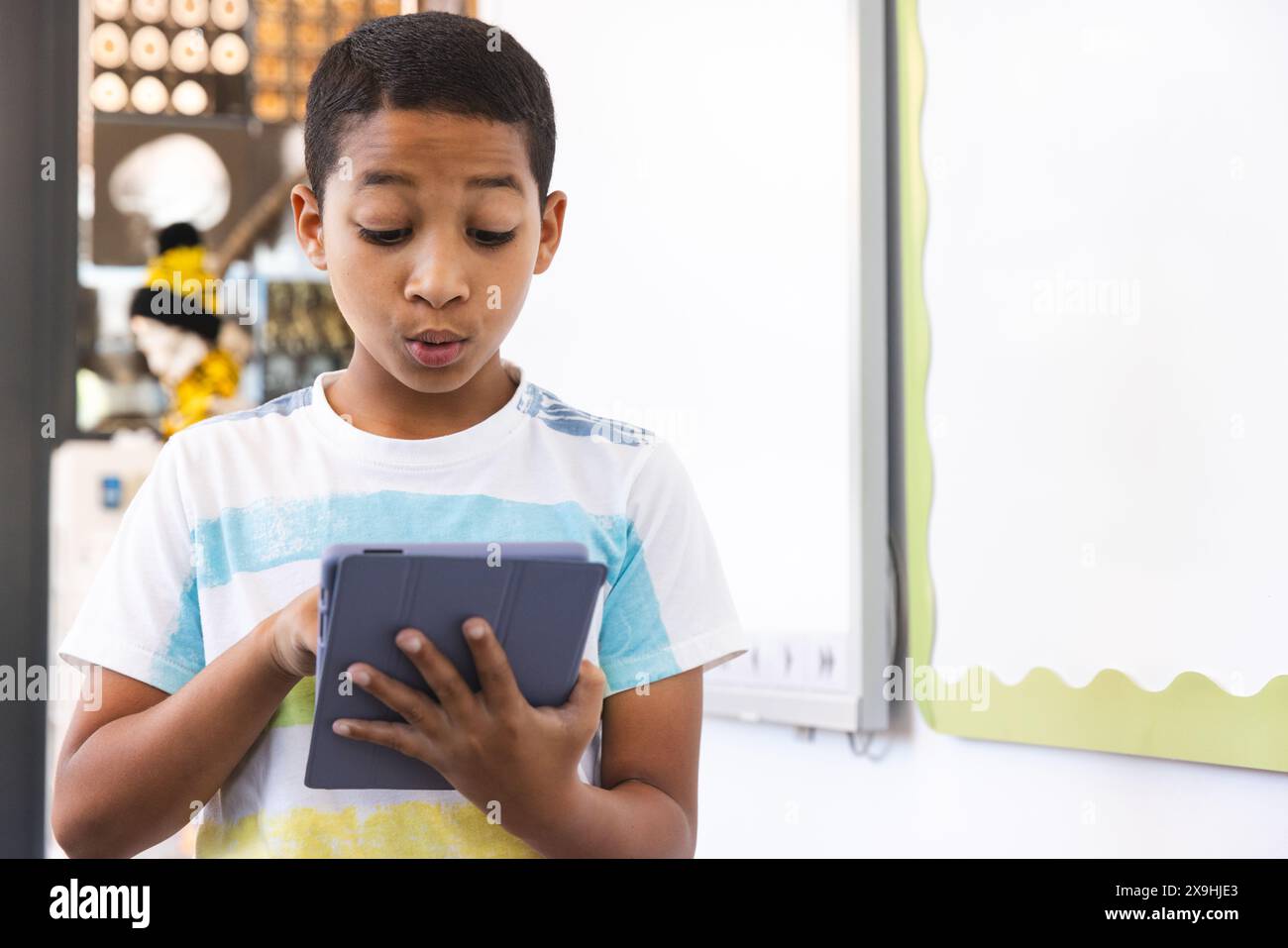 Ein birassischer Junge sieht überrascht aus, wenn ein Tablet in einem hellen Schulzimmer steht Stockfoto