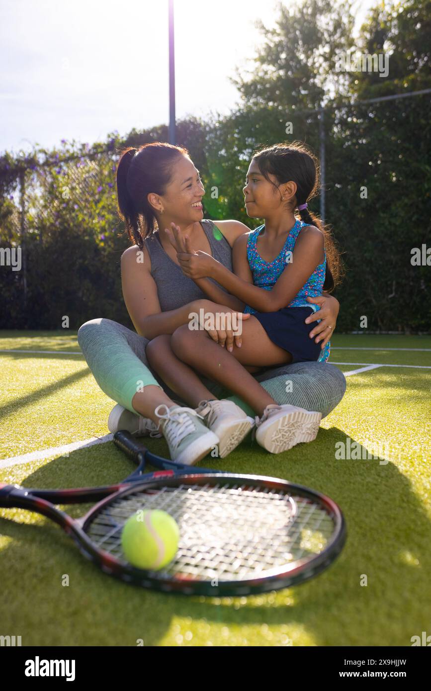 Draußen sitzen Mutter und Tochter auf dem Tennisplatz und lächeln sich gegenseitig an Stockfoto