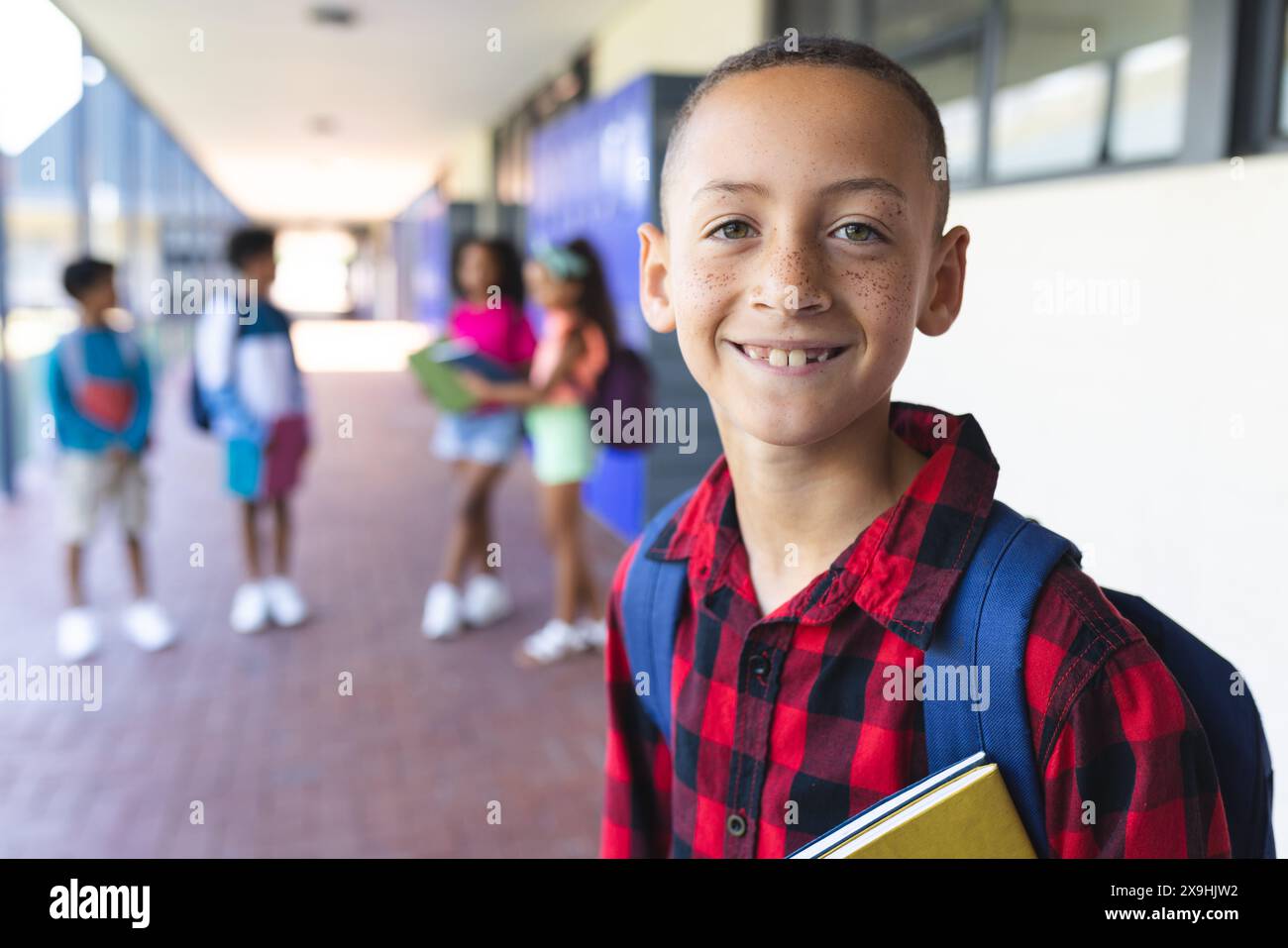 Ein birassischer Junge mit rotem kariertem Hemd und Rucksack lächelt in der Schule Stockfoto