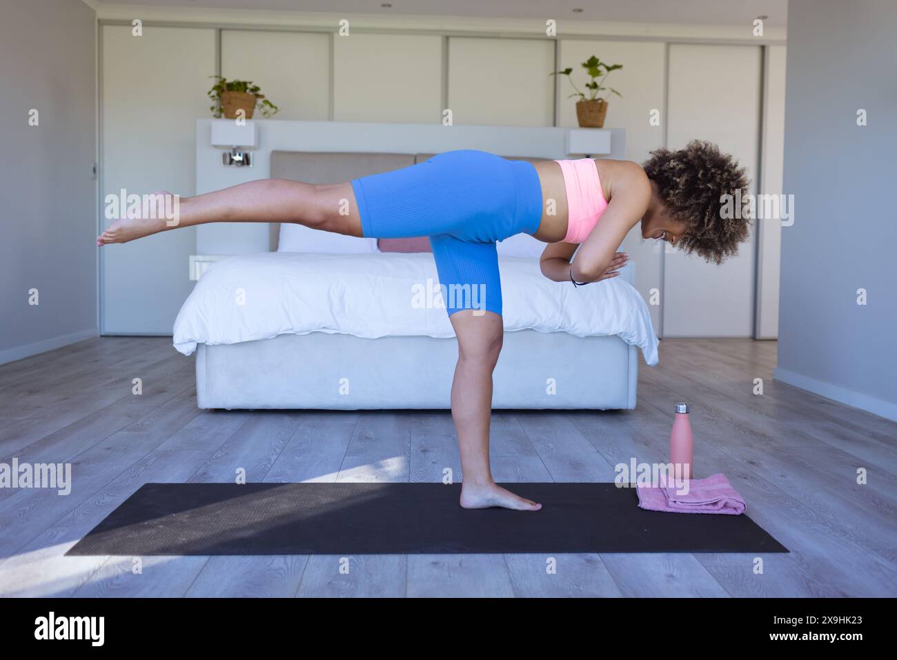 Zu Hause übt eine junge Frau mit blauer Leggings und rosa Oberteil Yoga Stockfoto