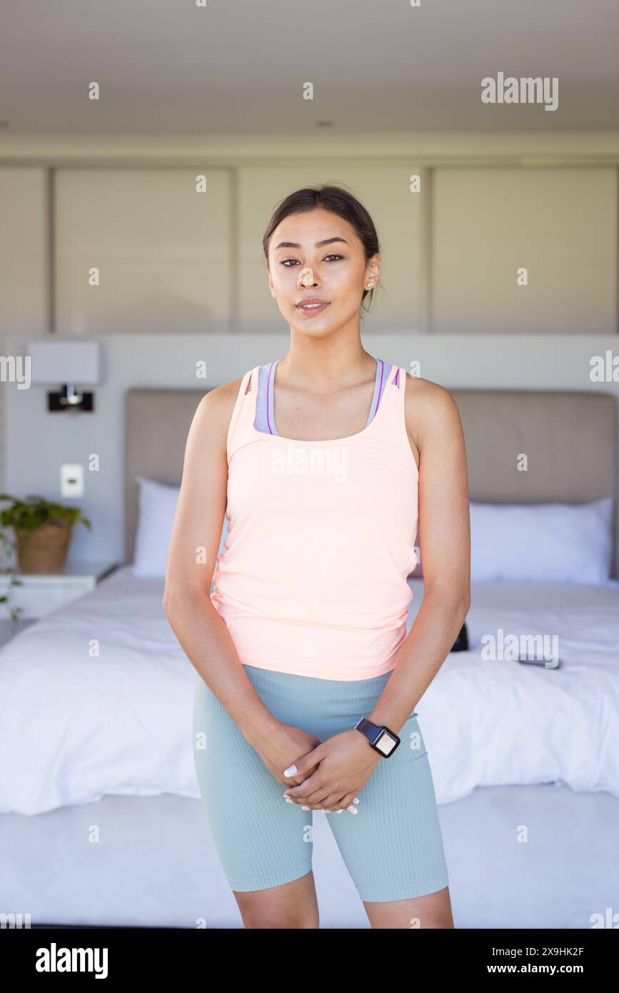 Zu Hause, zweirassige junge Frau in Fitnesskleidung, stehend im Schlafzimmer Stockfoto