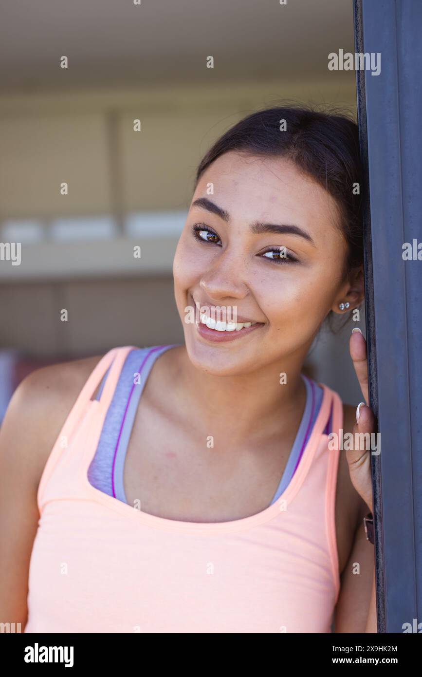 Eine zweirassige junge Frau zu Hause, die sich in einem rosafarbenen Oberteil an die Tür lehnt Stockfoto