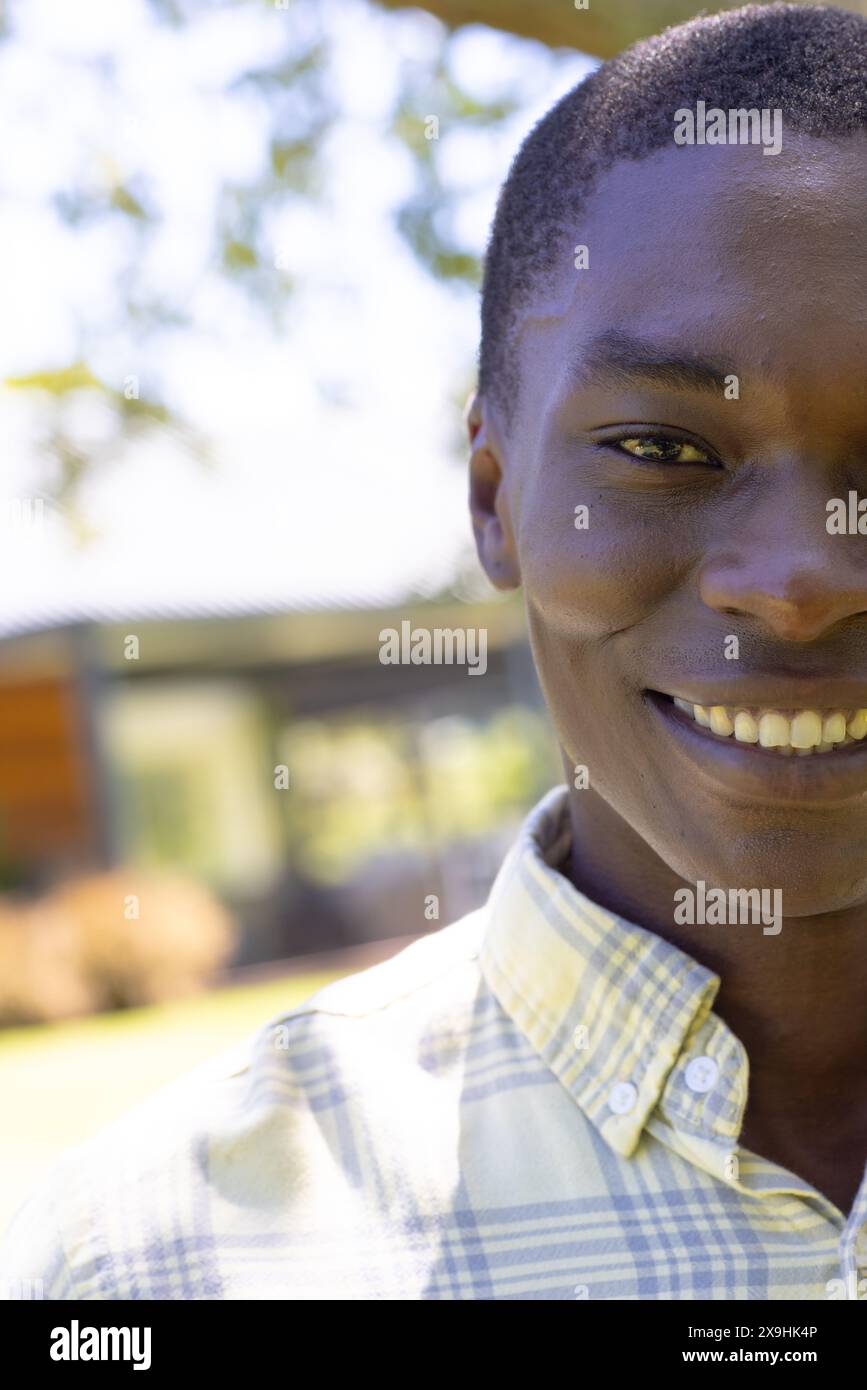 Ein junger Afroamerikaner, der kariertes Hemd trägt, draußen lächelt, Kopierraum Stockfoto