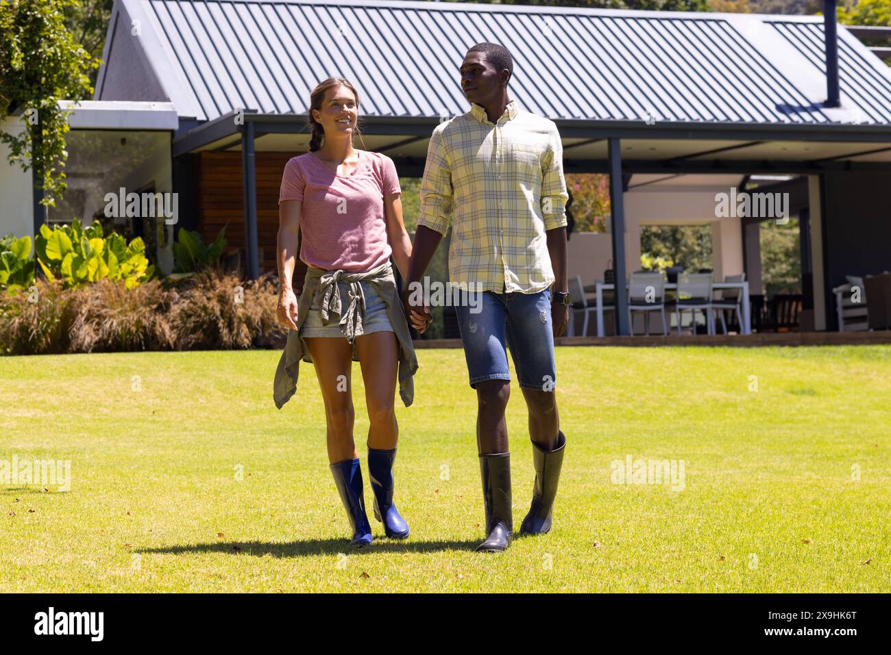 Ein vielfältiges junges Paar, das draußen im sonnigen Garten spaziert Stockfoto