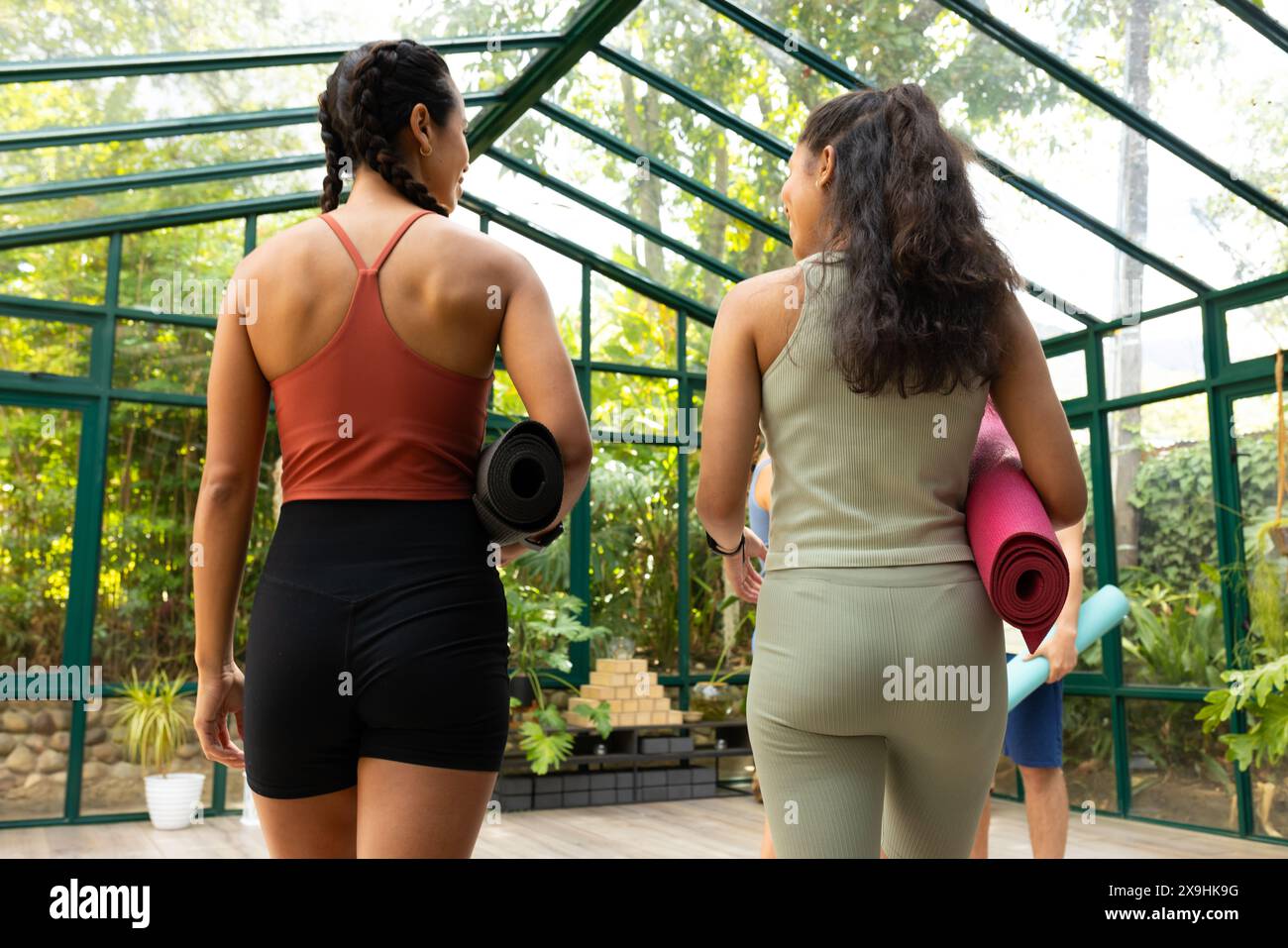 Verschiedene Yoga-Studentinnen, die im Glashaus-Studio spazieren gehen Stockfoto