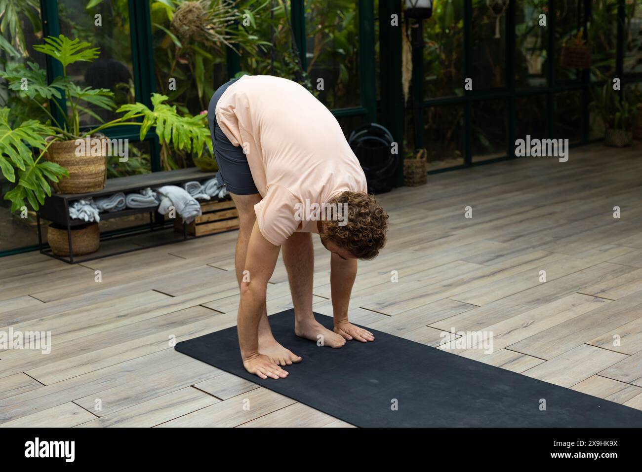 Das Glashaus-Studio fängt kaukasische männliche Yogalehrer ein, die sich auf der Matte beugt Stockfoto