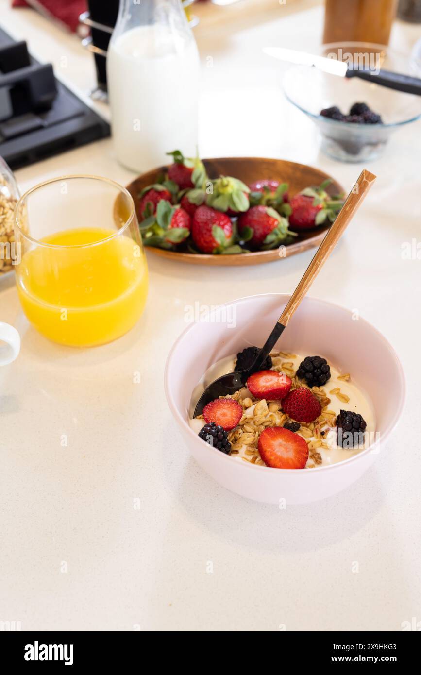 Frühstück: Schüssel Müsli mit Joghurt, Erdbeeren und Brombeeren, Kopierraum. Orangensaft im Glas, Milchflasche und Teller Erdbeeren Stockfoto