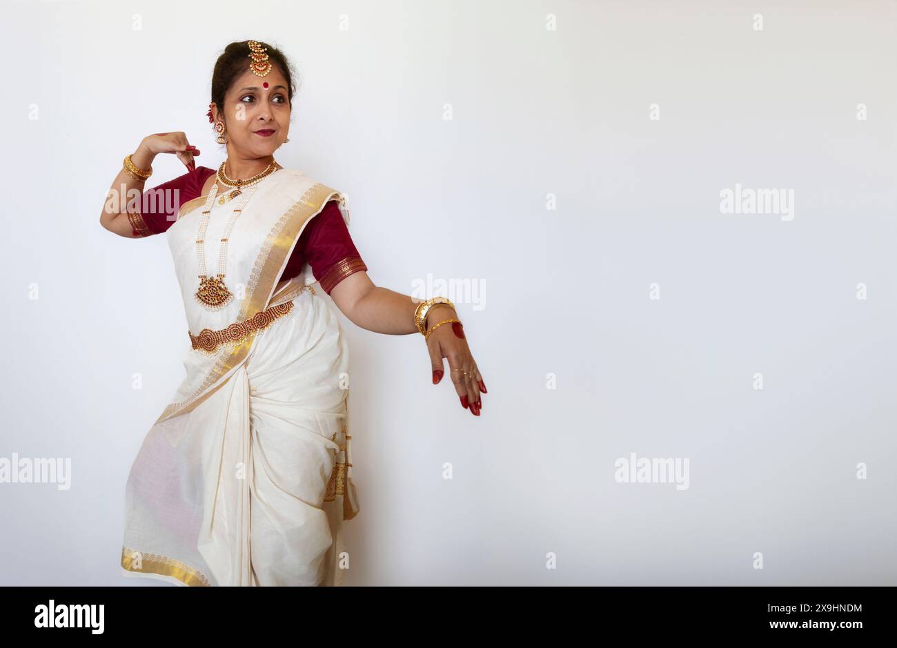 Klassische indische Tänzerin in traditionellem Tanzkostüm, die Bharatanatyam-Tanzposition (Mudra) auf hellem Hintergrund mit Kopierraum demonstriert. Stockfoto
