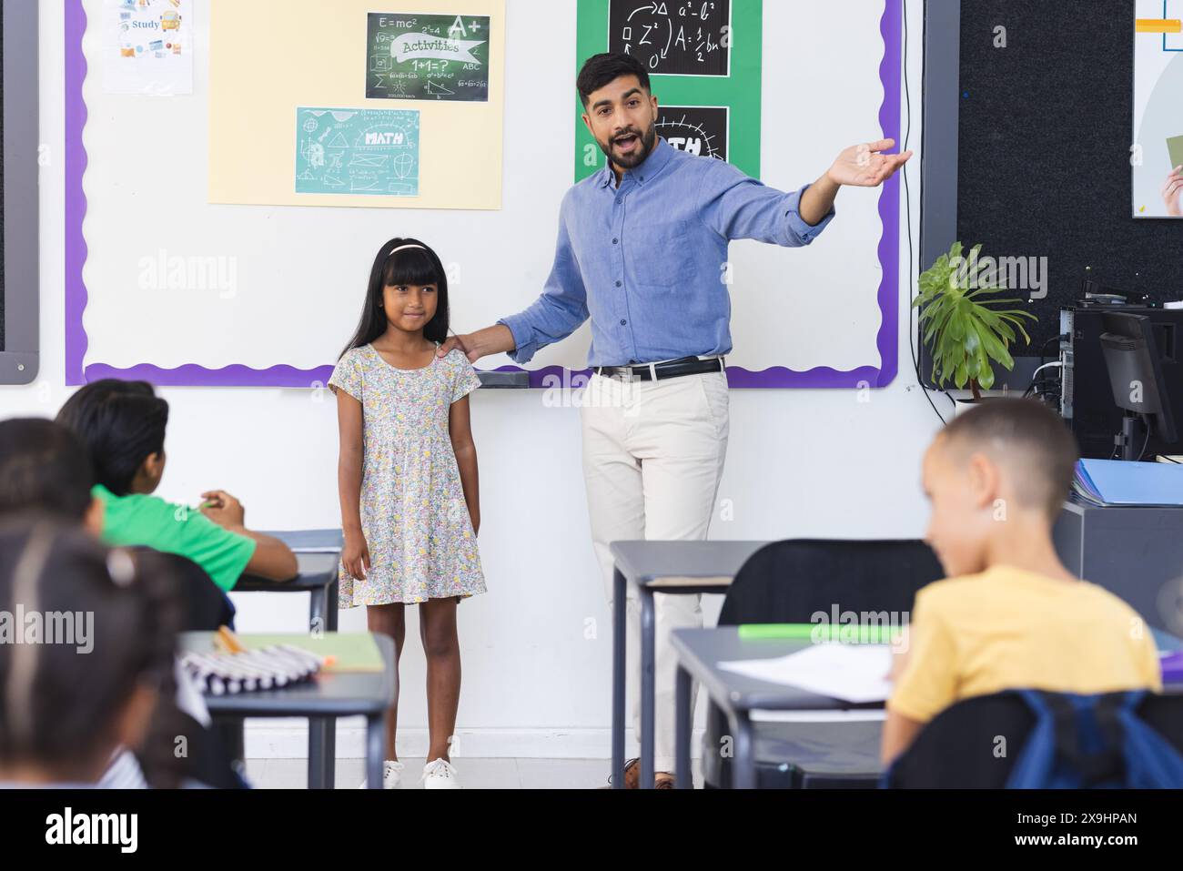 Ein junger asiatischer Lehrer stellt ein birassisches Mädchen in einem Klassenzimmer vor Stockfoto