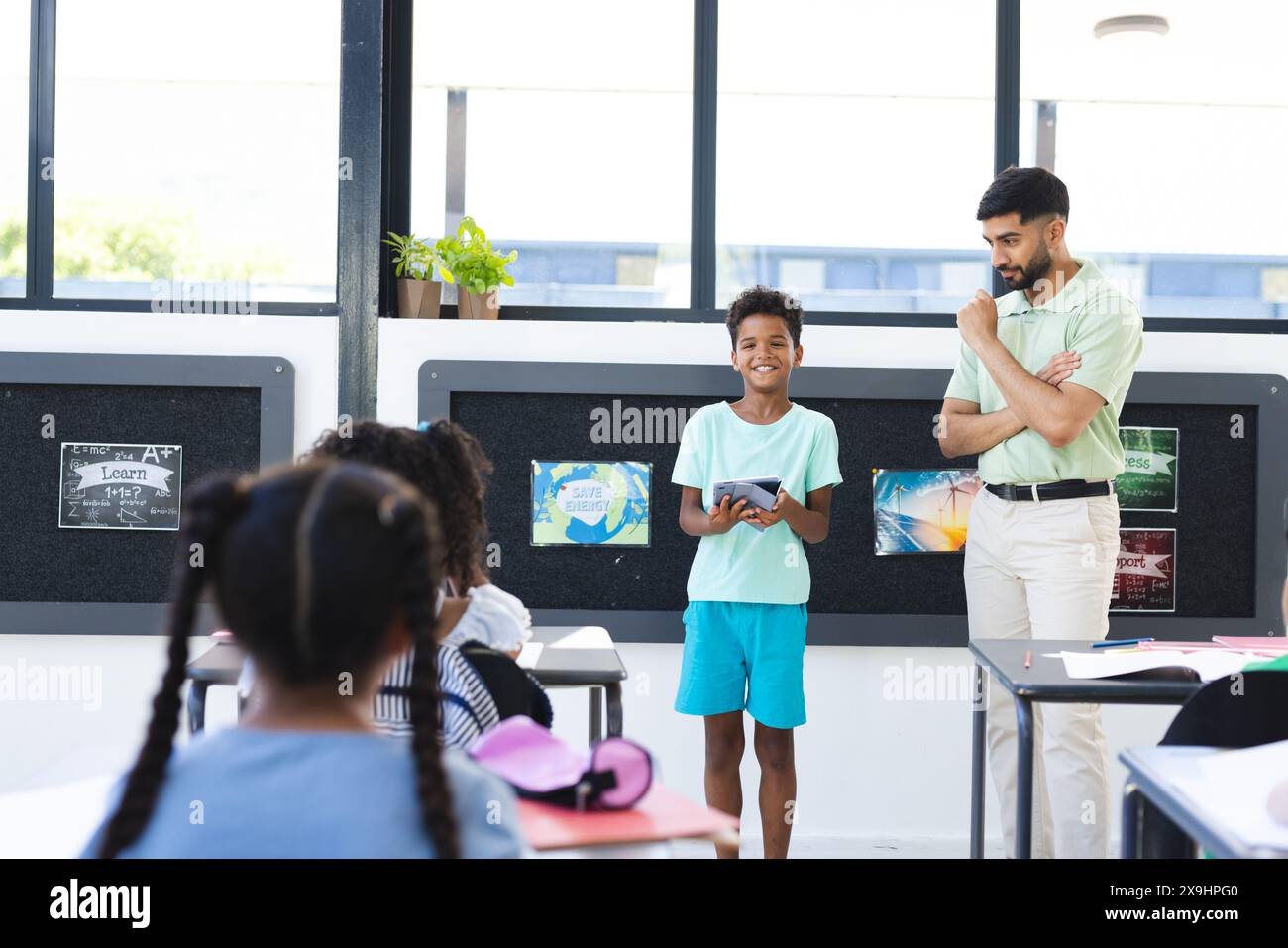 In der Schule beobachtete ein männlicher asiatischer Lehrer, wie ein männlicher Schüler mit einer Tablette in der Hand war Stockfoto