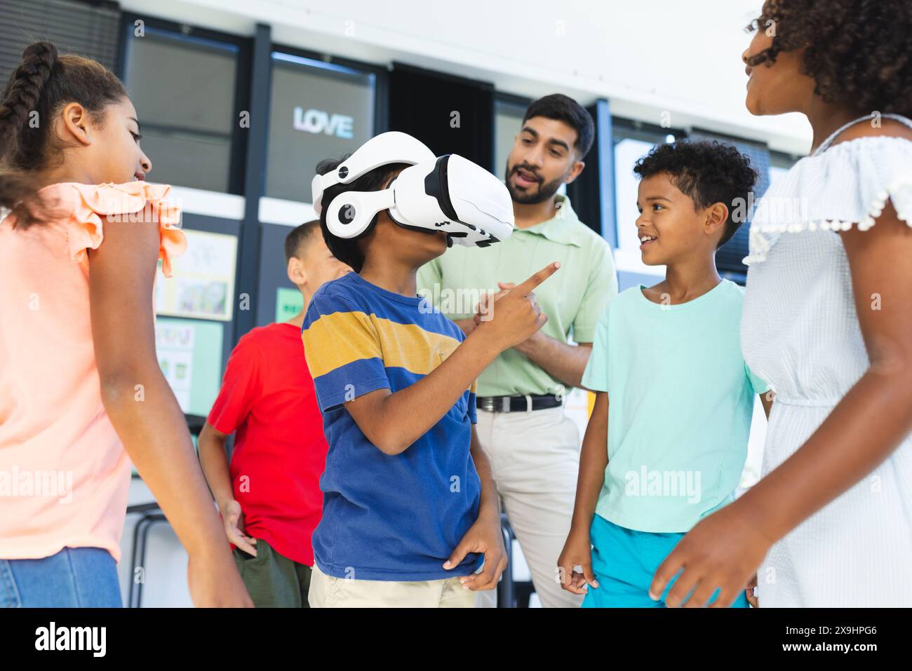 In der Schule schauen sich junge asiatische Lehrer und verschiedene Schüler eine VR-Brille an Stockfoto