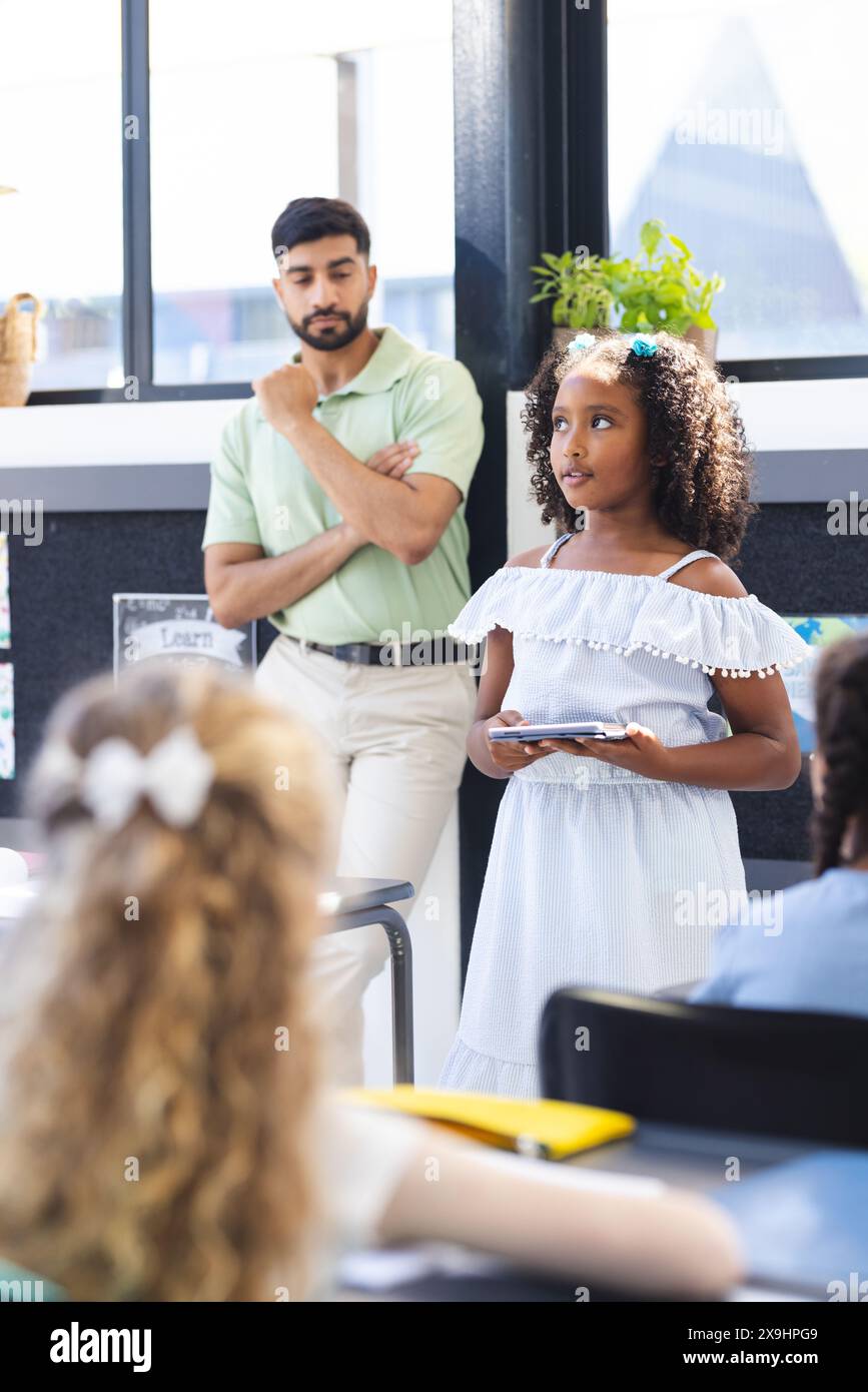In der Schule sieht ein asiatischer Lehrer zu, wie eine birassische Schülerin präsentiert Stockfoto