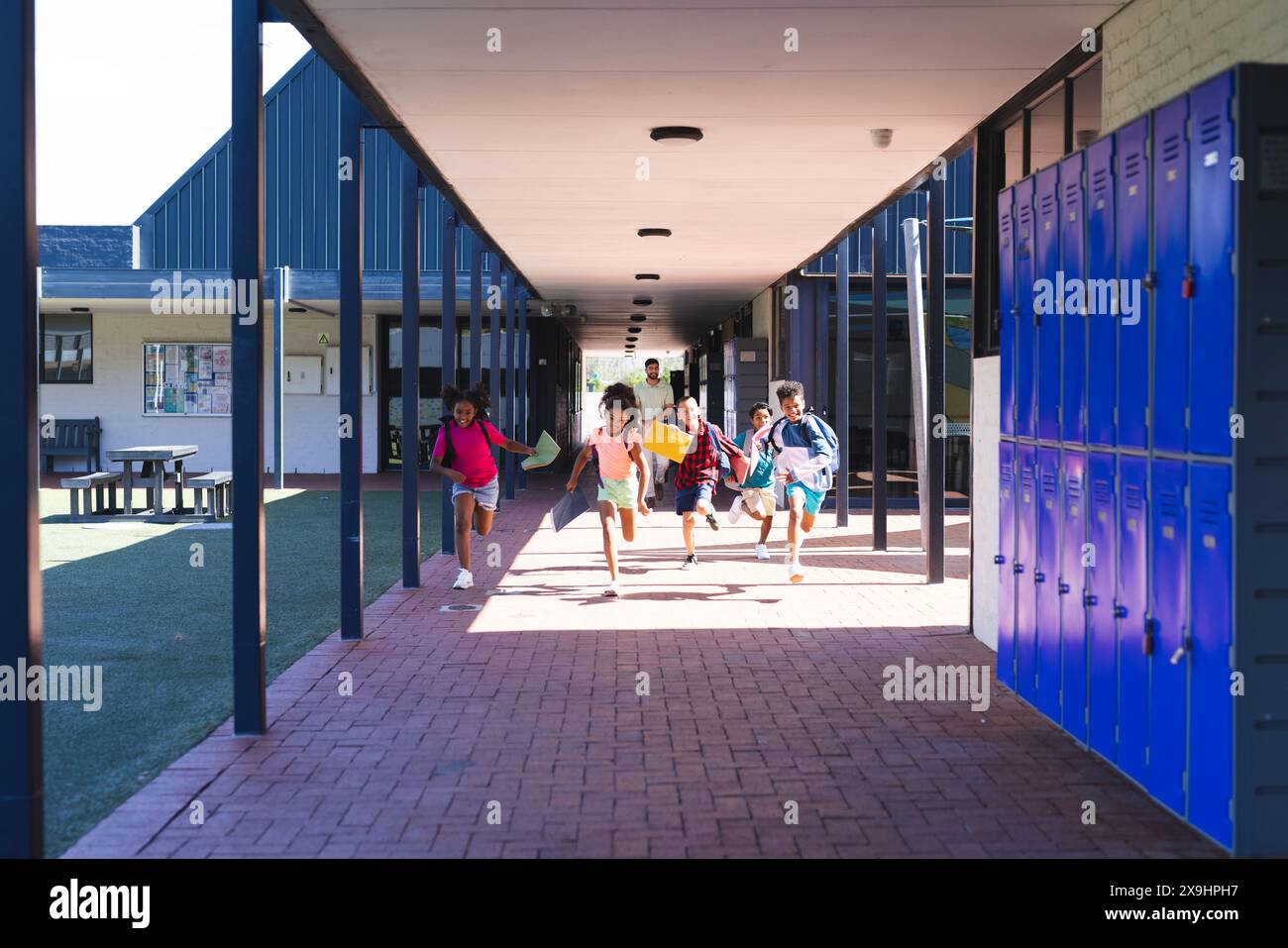Aufgeregte Kinder laufen durch einen Schulflur, Schließfächer säumen die Wand mit Kopierraum Stockfoto