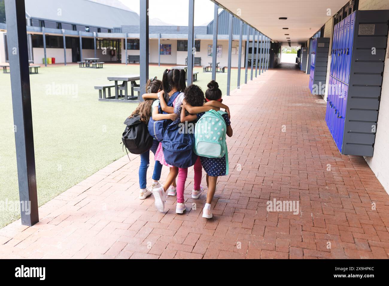 In der Schule laufen vier junge, birassische Mädchen im Freien eng zusammen Stockfoto