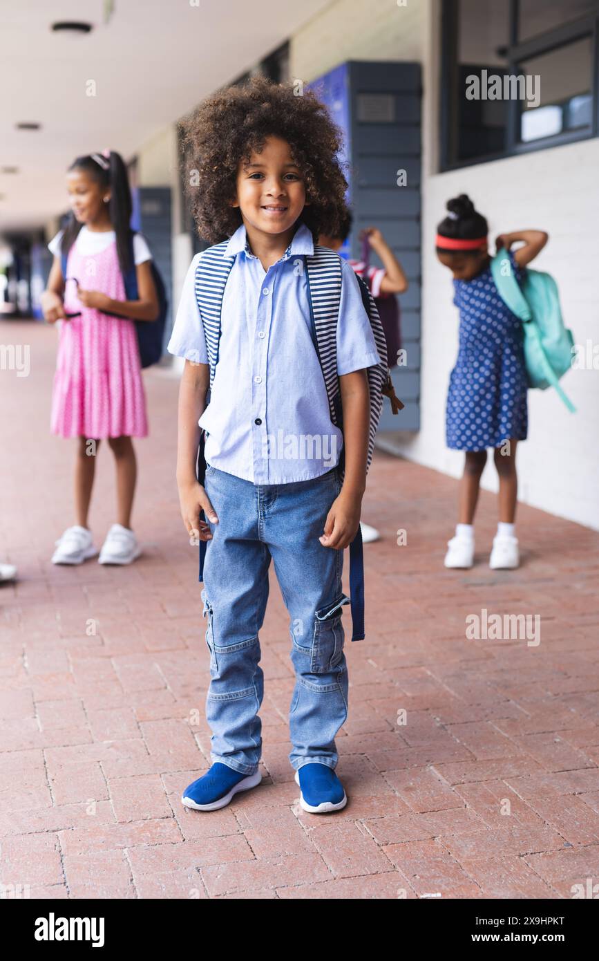 In der Schule steht ein junger afroamerikanischer Junge im Freien und lächelt mit einem Rucksack Stockfoto