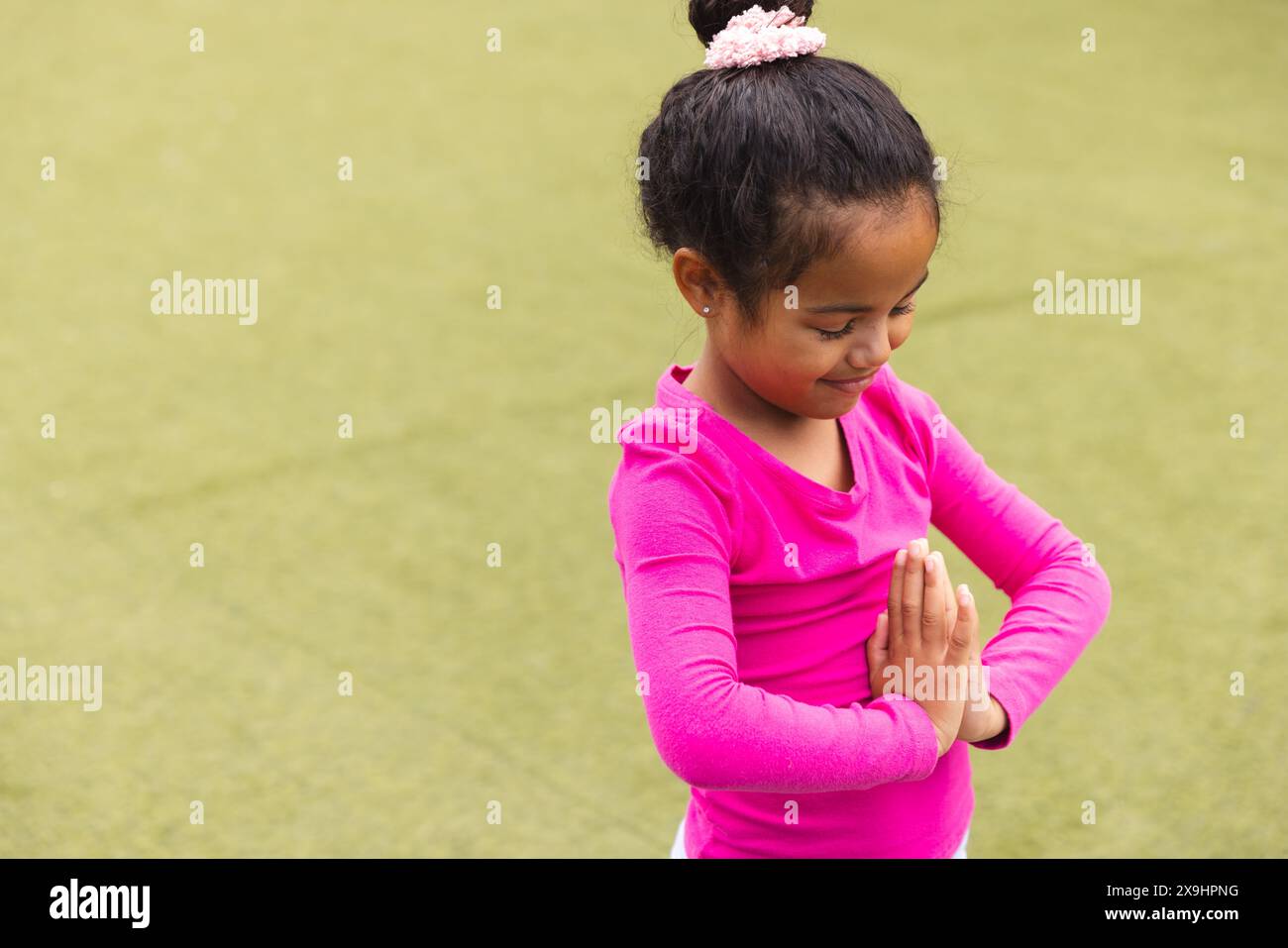 In der Schule praktiziert ein junges birassisches Mädchen in Rosa im Freien Yoga mit Kopierraum Stockfoto