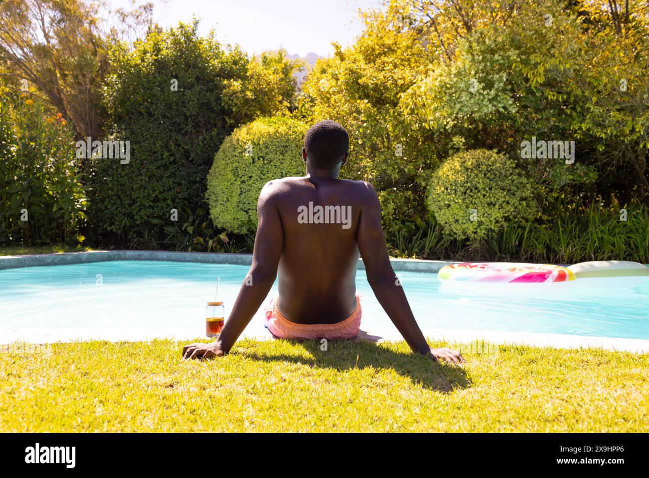 Ein junger Mann aus Afroamerikaner, der draußen sitzt und rosa Badeshorts trägt Stockfoto