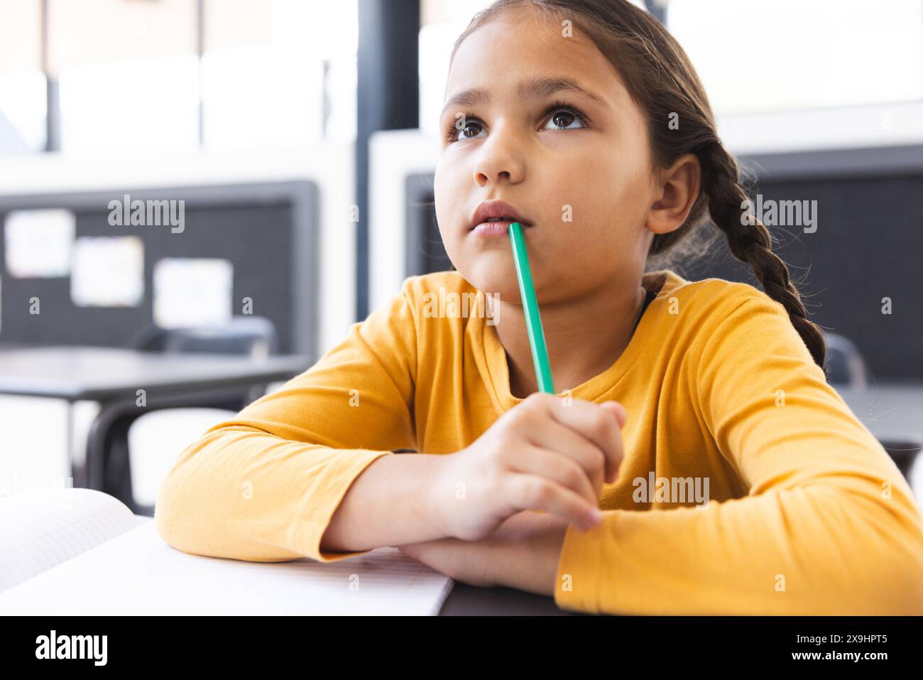 In der Schule, im Klassenzimmer, ein junges birassisches Mädchen, das einen Bleistift hält und nachdenklich aussieht Stockfoto