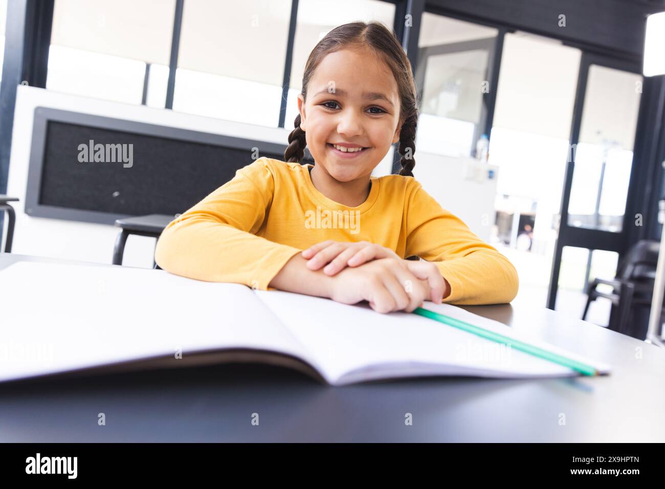 In der Schule saß eine junge birassische Schülerin am Schreibtisch in einem Klassenzimmer und lächelte Stockfoto
