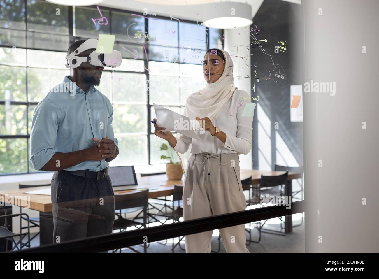 In modernen Geschäftsbüros arbeiten verschiedene Teams zusammen. Afroamerikanischer Mann mit VR-Headset, indische Frau hält Dokumente, diskutiert Ideen wr Stockfoto