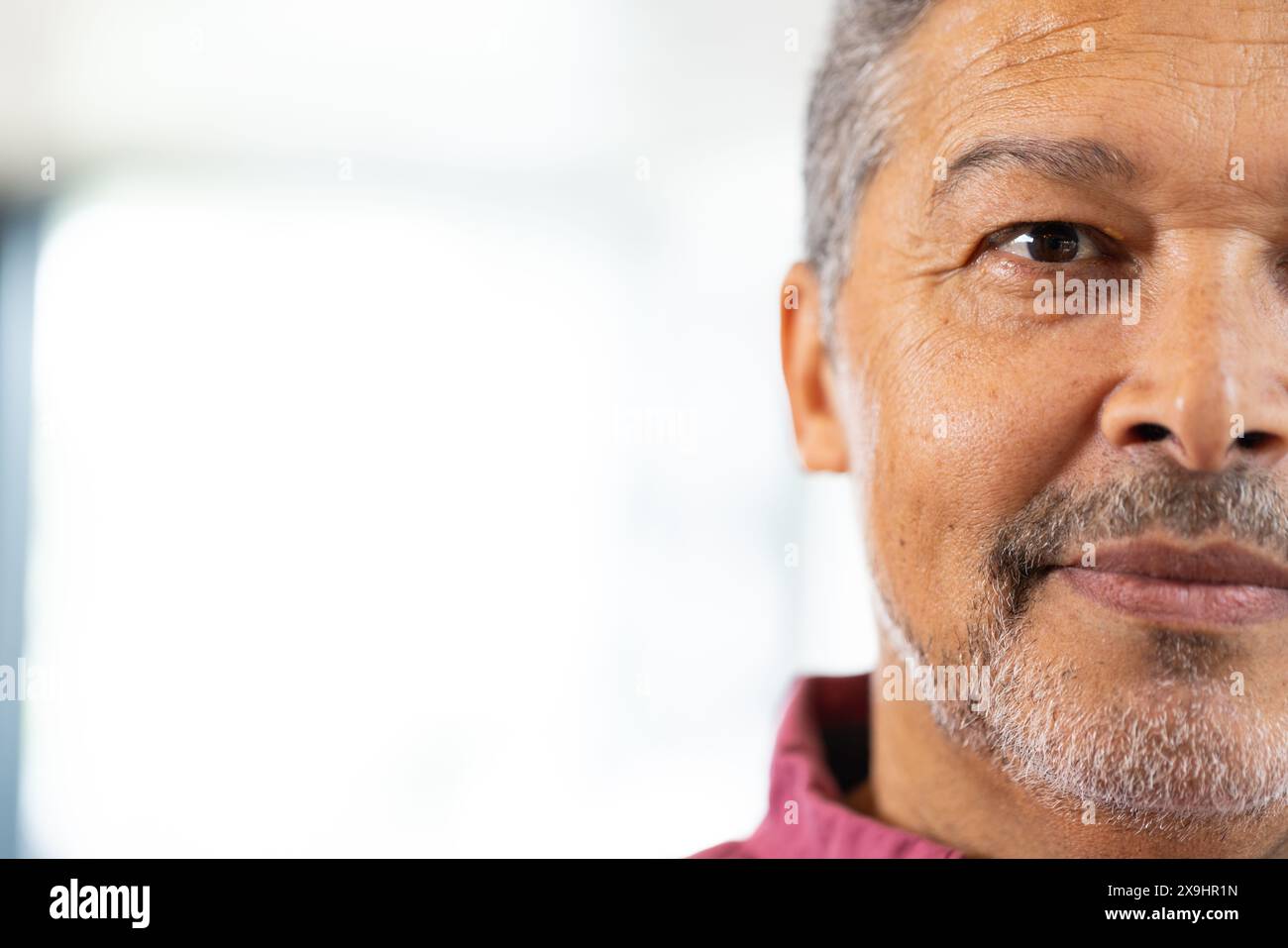 Zu Hause, zweirassiger älterer Mann mit kurzen grauen Haaren und Bart, der in die Kamera schaut, Kopierraum. Mit rotem Hemd, verschwommenem Hintergrund mit natürlichem Licht Stockfoto