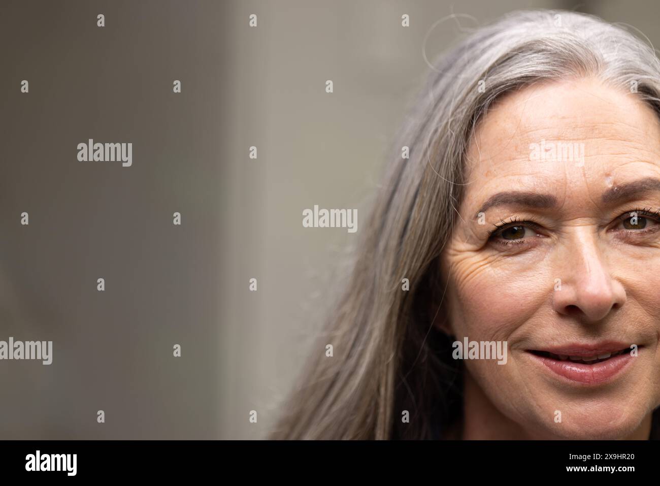 Zu Hause eine ältere Weibchen mit langen grauen Haaren, die sanft in die Kamera lächelt, im Kopierraum Stockfoto