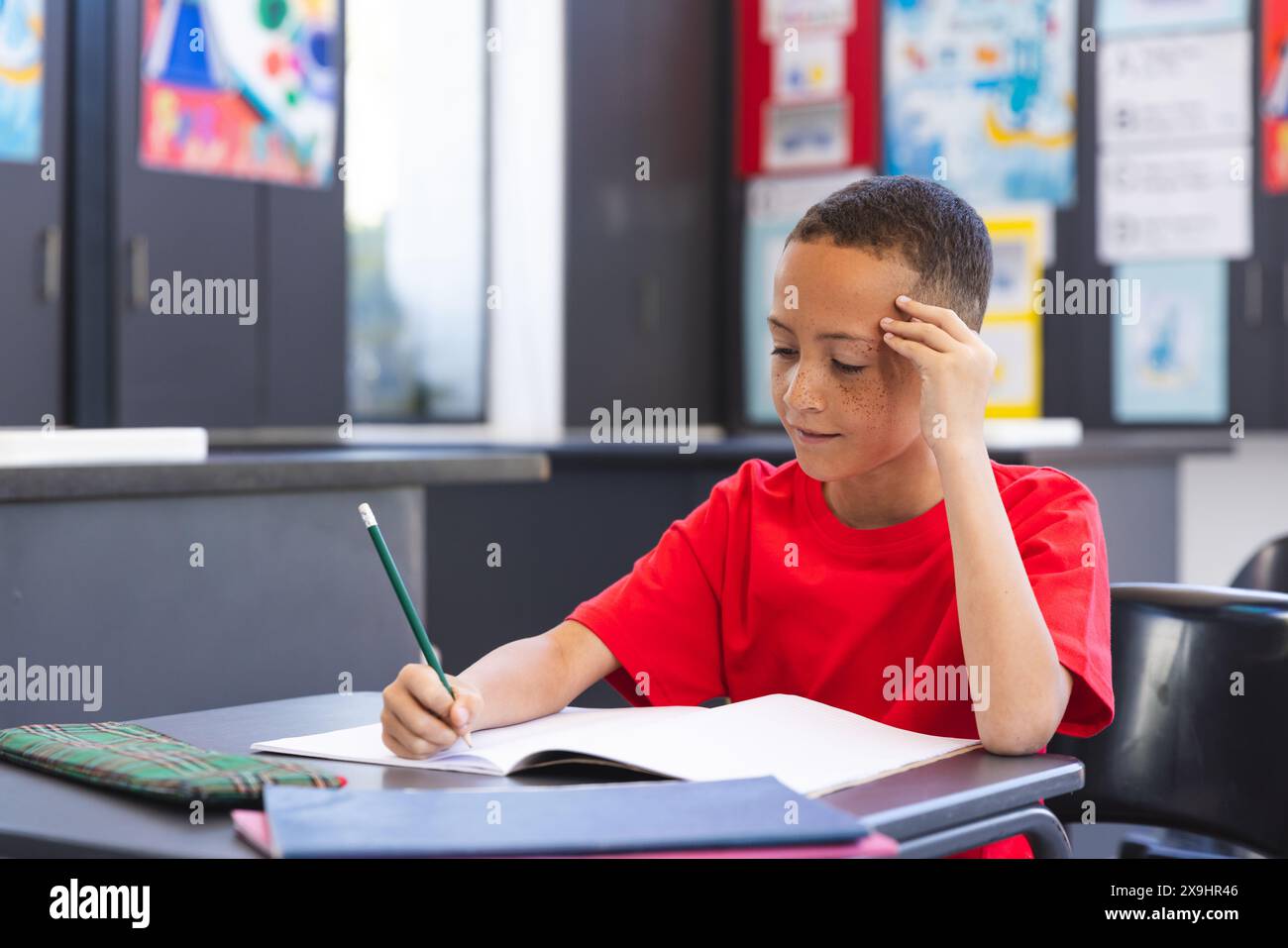 Biracial Boy konzentriert sich auf seine Schularbeit in einem Klassenzimmer in der Schule Stockfoto