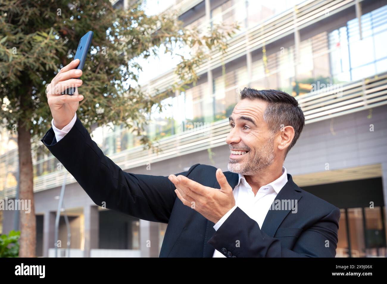 Porträt eines lächelnden Geschäftsmannes, der draußen ein Foto mit einem Smartphone macht. Stockfoto