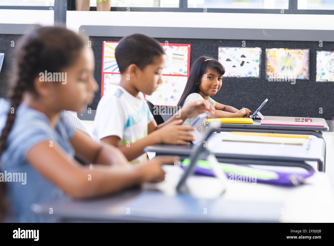 In der Schule konzentrieren sich drei junge birassische Schüler auf ihre Aufgaben im Klassenzimmer Stockfoto