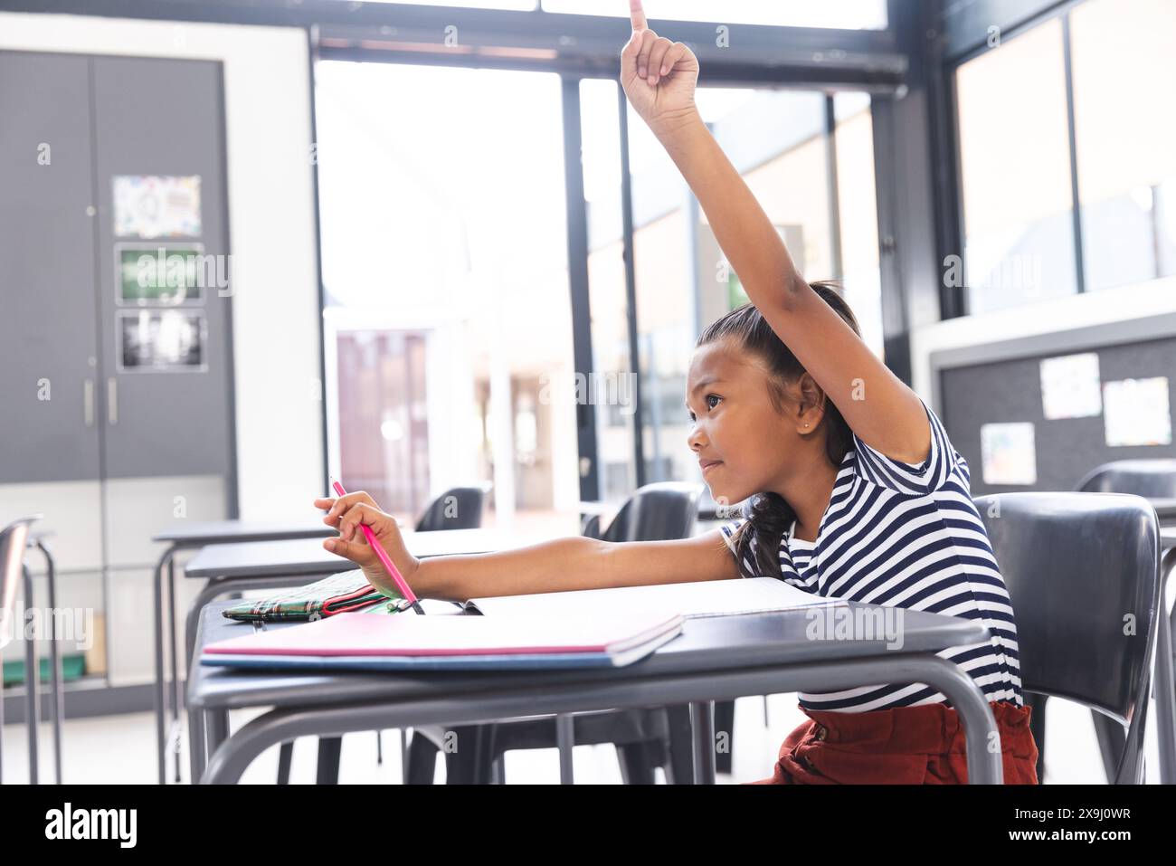 Birassisches Mädchen mit heller Haut, dunklem Haar hebt die Hand in der Klasse, Kopierraum Stockfoto