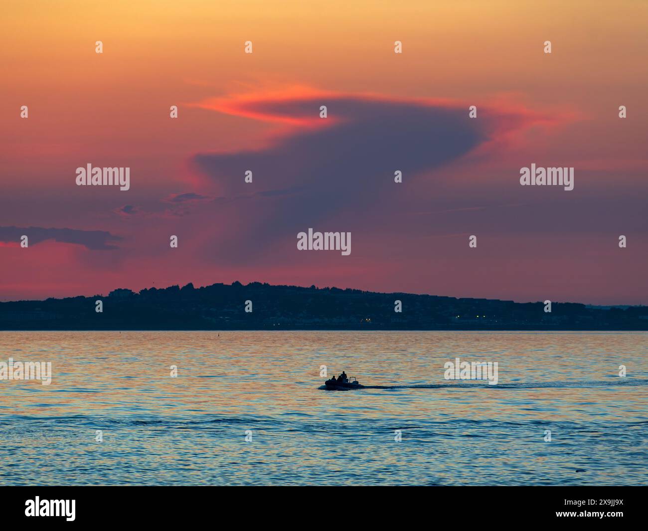 Kleines Boot, das an einer fernen Gewitterwolke bei Sonnenuntergang von Howth vorbeifährt Stockfoto